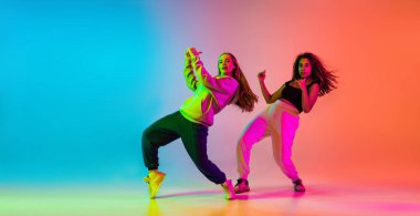 İki güzel hip-hop dansçısı renkli arka planda neon ışıklarıyla dans ediyorlar.