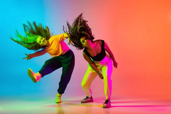 Dos hermosas chicas de hip-hop bailando en gradiente fondo naranja azul en neón — Foto de Stock