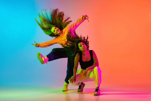 Dos hermosas chicas de hip-hop bailando en gradiente fondo naranja azul en neón — Foto de Stock