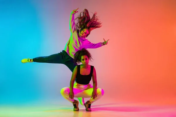 Дві красиві хіп-хоп дівчата танцюють на градієнтному синьому помаранчевому фоні в неоні — стокове фото