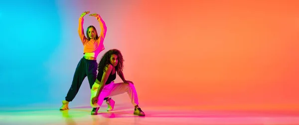 Two beautiful stylish hip-hop female dancers on colorful gradient background in neon lights — Stock Photo, Image