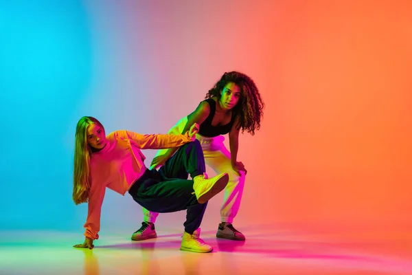 Rhytm. Due ragazze moderne alla moda che ballano hip-hop su sfondo blu arancio sfumato al neon — Foto Stock