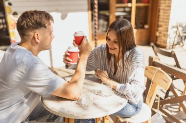 Genç ve güzel bir çiftin parlak bir yaz gününde kafede oturup birlikte kahvenin tadını çıkarırken çekilmiş portresi.