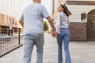 Yazın güneşli bir günde şehirde yürüyen mutlu genç bir çiftin arkasından kesilmiş portre.
