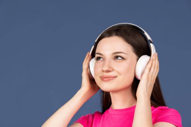 Koyu mavi arka planda müzik dinleyen güzel beyaz bir kadın.