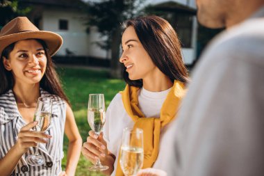 Kırsalda arkadaşlarıyla bir bardak şampuanla dinlenen iki genç kadının kesilmiş portresi.