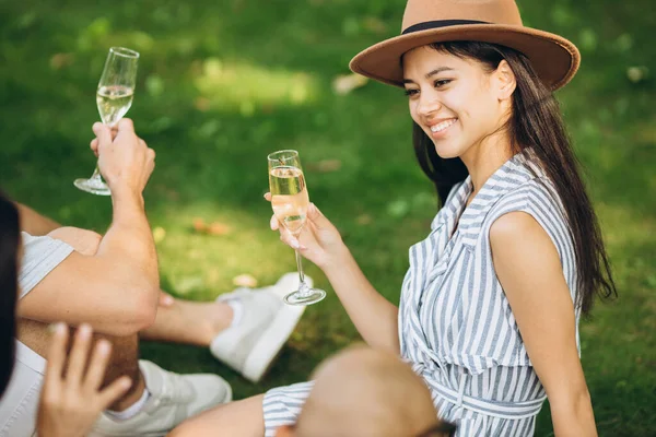 Jedna piękna dziewczyna w kapeluszu siedzi ze szklanką szampana i spędza czas z przyjaciółmi — Zdjęcie stockowe