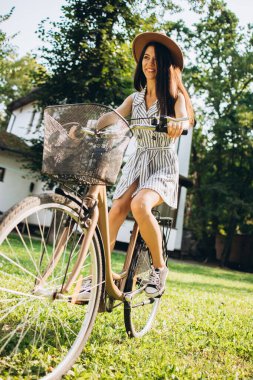 Sıcak bir yaz gününde bahçede bisiklete binen güzel bir kızın tam boy portresi.