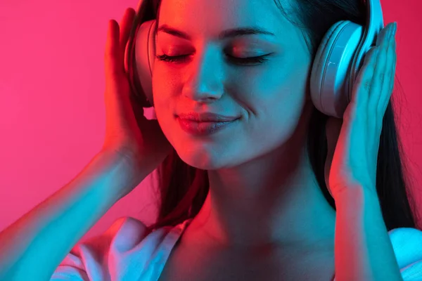 Detailní oříznutý portrét mladé krásné dívky se sluchátky na gradient růžové červené studio pozadí — Stock fotografie