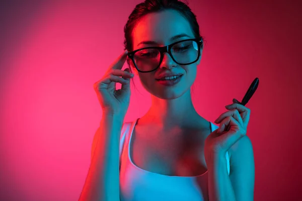 Retrato recortado de menina bonita jovem em óculos no gradiente rosa fundo vermelho — Fotografia de Stock