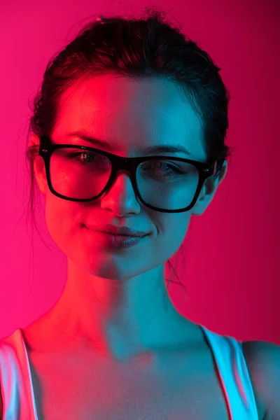 Close-up recortado retrato de menina bonita jovem em óculos em gradiente rosa fundo vermelho em luzes de néon — Fotografia de Stock