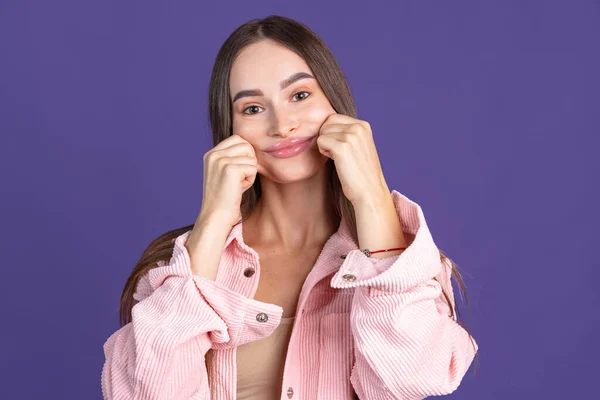 Ritagliato primo piano ritratto di giovane bella donna che fa facce divertenti sulla macchina fotografica isolata su sfondo viola — Foto Stock
