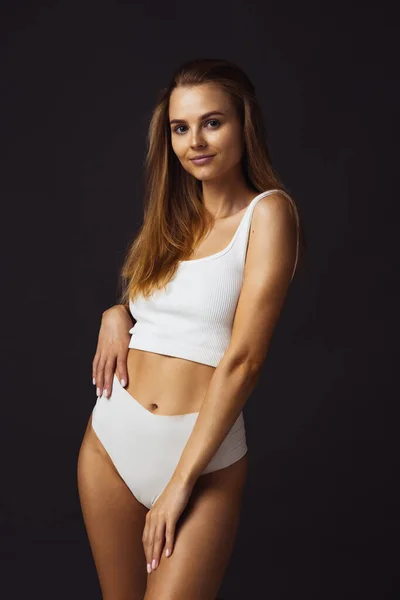 Eine junge schöne kaukasische Frau in weißer Unterwäsche auf dunklem Studiohintergrund — Stockfoto