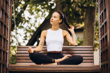 Açık havada meditasyon yapan genç, ince, beyaz bir kızın tam boy yatay portresi.