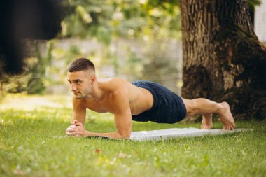 Sıcak bir yaz gününde dışarıda yoga yapan yakışıklı bir adamın tam boy portresi.