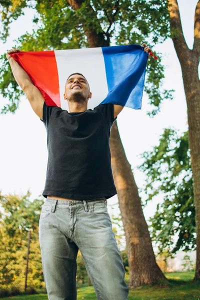 Onderaanzicht bijgesneden portret van jonge lachende man met vlag van Frankrijk geïsoleerd over natuurlijke achtergrond — Stockfoto