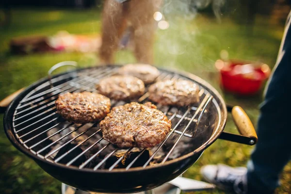 Close-up photo of burger cutlets on grill. Tasty food cooking. Friends picnic on warm summer day — Stock Photo, Image