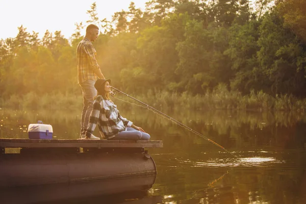 Giovane coppia pesca sul molo al tramonto nella calda giornata estiva — Foto Stock