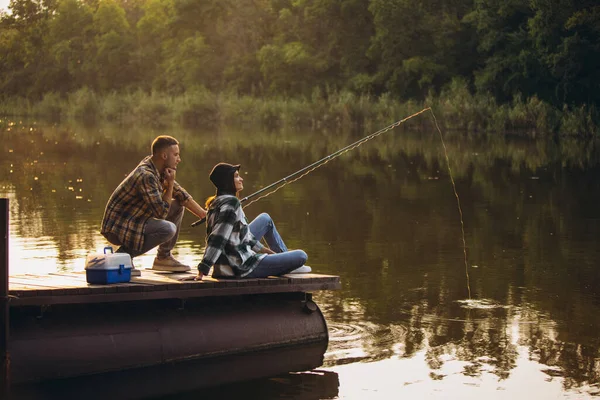 Giovane coppia pesca sul molo al tramonto nella calda giornata estiva — Foto Stock