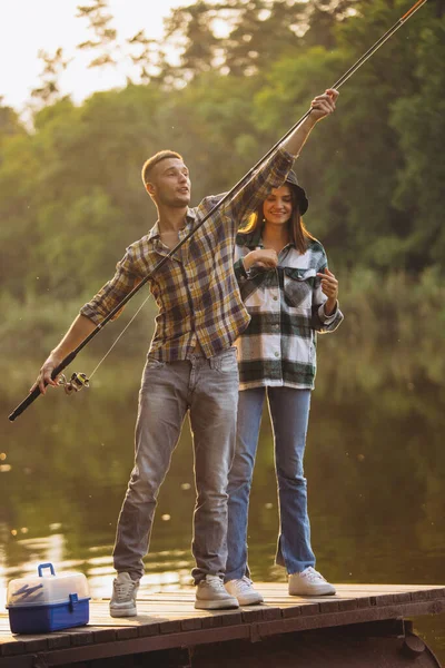 Retrato de pareja joven pescando en el lago en el cálido día de verano en el campo al atardecer — Foto de Stock