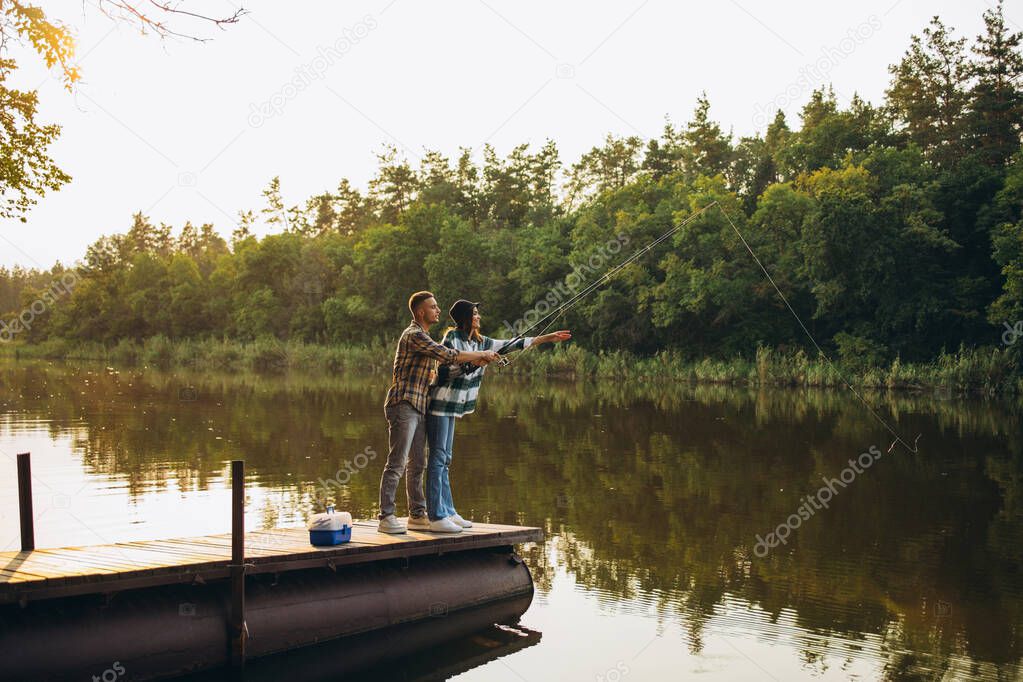 Full-length portrait of young couple fishing on warm summer day in countryside in early morning