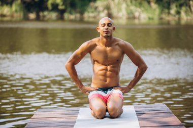 Sıcak yaz gününde iskelede meditasyon yapan yakışıklı bir adamın tam boy yatay portresi.