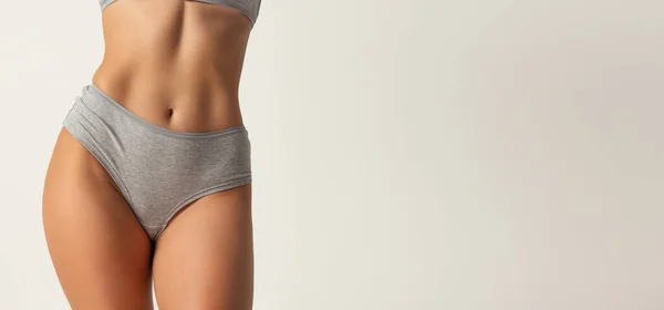 Detail oříznuté ženské tělo, břicho v šedém spodním prádle přes šedé pozadí. — Stock fotografie