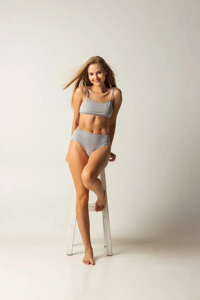 Full-length portrait of young caucasian woman in gray inner wear isolated over grey studio background — Stock Photo, Image