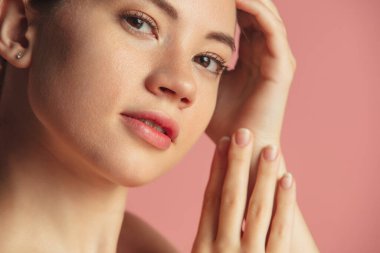 Pembe arka planda izole edilmiş kameraya nazikçe bakan güzel bir kadının yakın plan portresi.