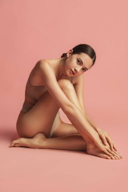 Doğal güzellik. Pembe arka planda soyutlanmış, iç çamaşırlı, genç ve zayıf bir kadının uzun bir portresi.