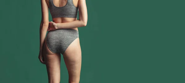 Gestutzter weiblicher Körper in grauer Baumwollunterwäsche über grünem Hintergrund. Rückenansicht Körper — Stockfoto