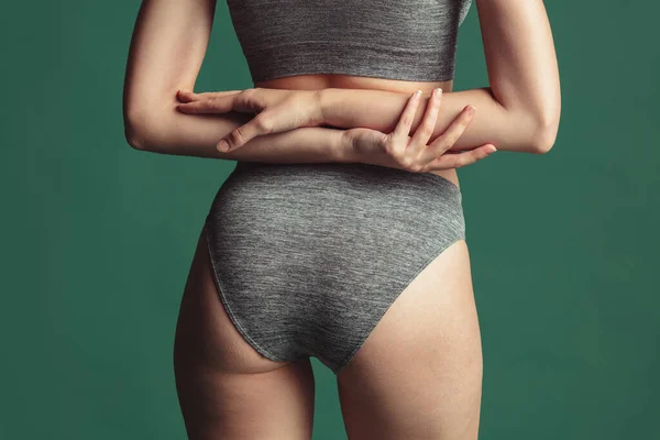 Närbild beskärd bild av passform kvinnlig kropp i grå bomull underkläder över grön bakgrund. Bakifrån — Stockfoto