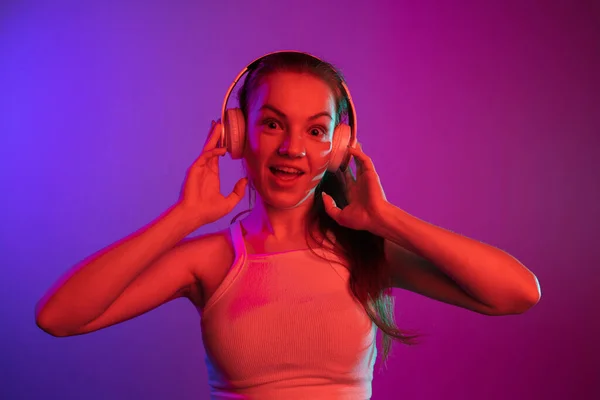 Portrait recadré d'une jeune fille joyeuse dans un casque écoutant de la musique isolée sur fond de dégradé dans des néons — Photo