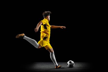 Genç bir adamın tam boy portresi, erkek futbolcu eğitimi siyah arka planda izole edilmiş. Yan görünüm