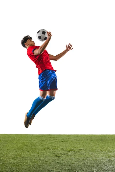 Retrato de comprimento total de jovem jogador de futebol masculino bola de limpeza com peito em um salto sobre o piso de grama fundo branco — Fotografia de Stock