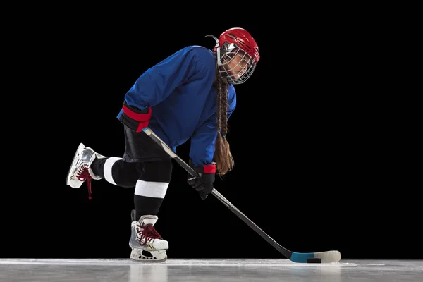 Full-length portrait of child girl, hockey player isolated over black background. Side view. Stickhandling