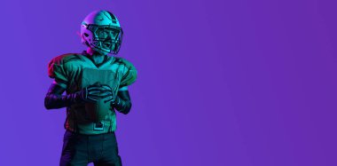 Amerikan futbolcusunun geniş açılı portresi koyu mor arka planda izole edilmiş.