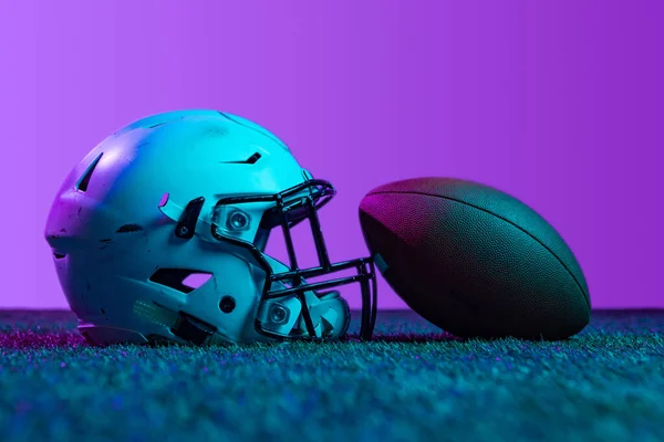 Estudio de tiro de equipo deportivo profesional para el juego de fútbol americano aislado sobre fondo púrpura en luces de neón. Casco y pelota — Foto de Stock