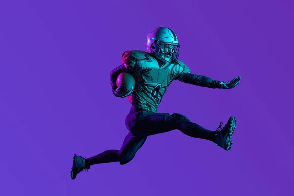 Full-délka portrét mužského amerického fotbalisty trénink izolovaný přes tmavě fialové pozadí studia — Stock fotografie