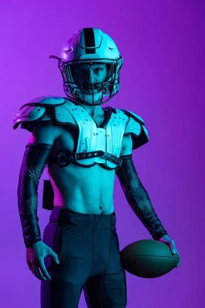 보라색 스튜디오 배경 위에 따로 떨어져 있는 헬멧 과 어깨 패드를 착용하고 있는 한 미국 프로 축구 선수의 초상화 — 스톡 사진