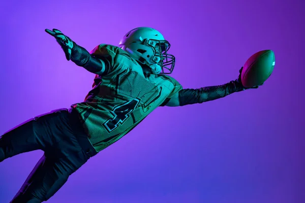 Un jugador de fútbol americano profesional en entrenamiento especial unofrm aislado sobre fondo de estudio púrpura. Entrenamiento de campeonato — Foto de Stock