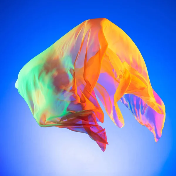 Elegante transparante veelkleurige vliegende stuk stof geïsoleerd over blauwe studio achtergrond — Stockfoto