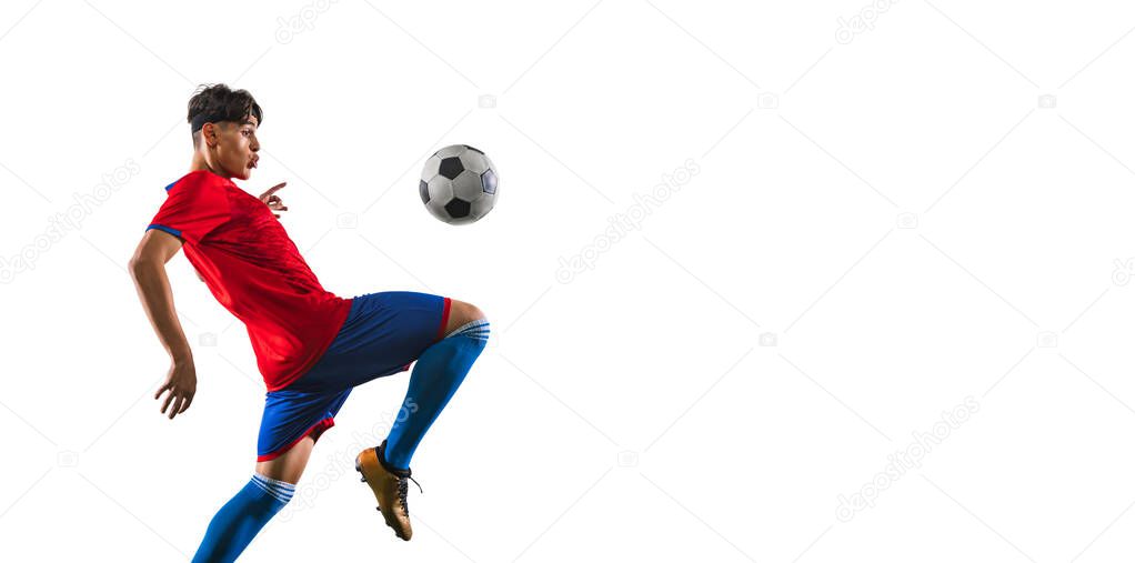 Cropped portrait in motion of male soccer football player kicking ball with knee on grass flooring white background