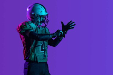 Yandan bakıldığında profesyonel Amerikan futbolcusunun görüntüsü mor stüdyo arka planında izole edilmiş.