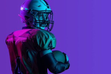 Arka planda, kasklı profesyonel Amerikan futbolcusunun mor arka planda izole edilmiş omuz yastığı ile çekilmiş görüntüsü var.