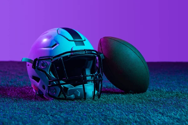 Estudio de tiro de equipo deportivo profesional para el juego de fútbol americano aislado sobre fondo púrpura en luces de neón. Casco y pelota — Foto de Stock