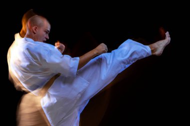 Siyah arka planda izole edilmiş genç karate sporcusu eğitiminin yan görüntüsü. Karışık ışık efekti