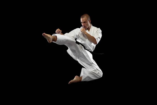 Full-length portrait. One young karate sportsman training isolated over black background