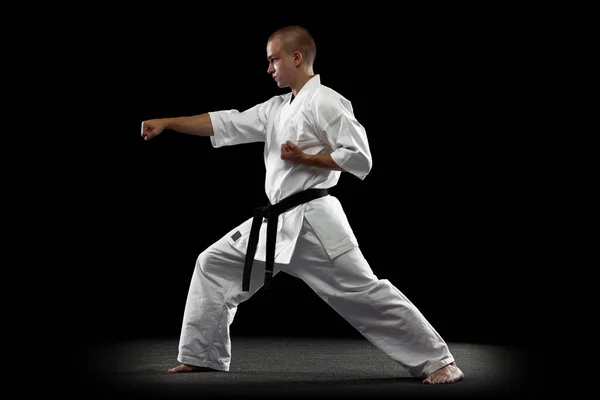 Full-length portrait of young sportsman, karateka, wearing white kimono isolated over black background — Stock Photo, Image