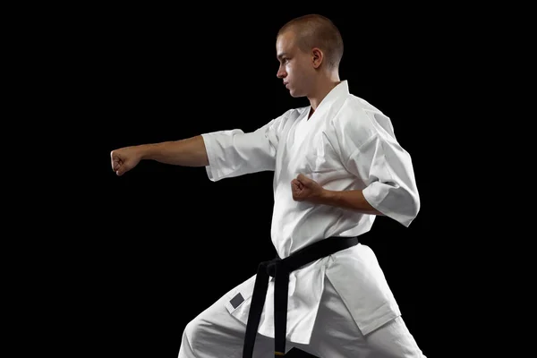 Teljes hosszúságú portré fiatal sportoló, karateka, viselt fehér kimono elszigetelt fekete háttér — Stock Fotó